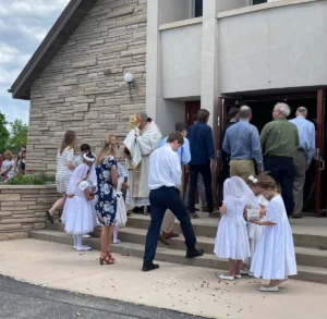 A priest carrying a golden monstrance down the aisle inside a church sanctuary.
